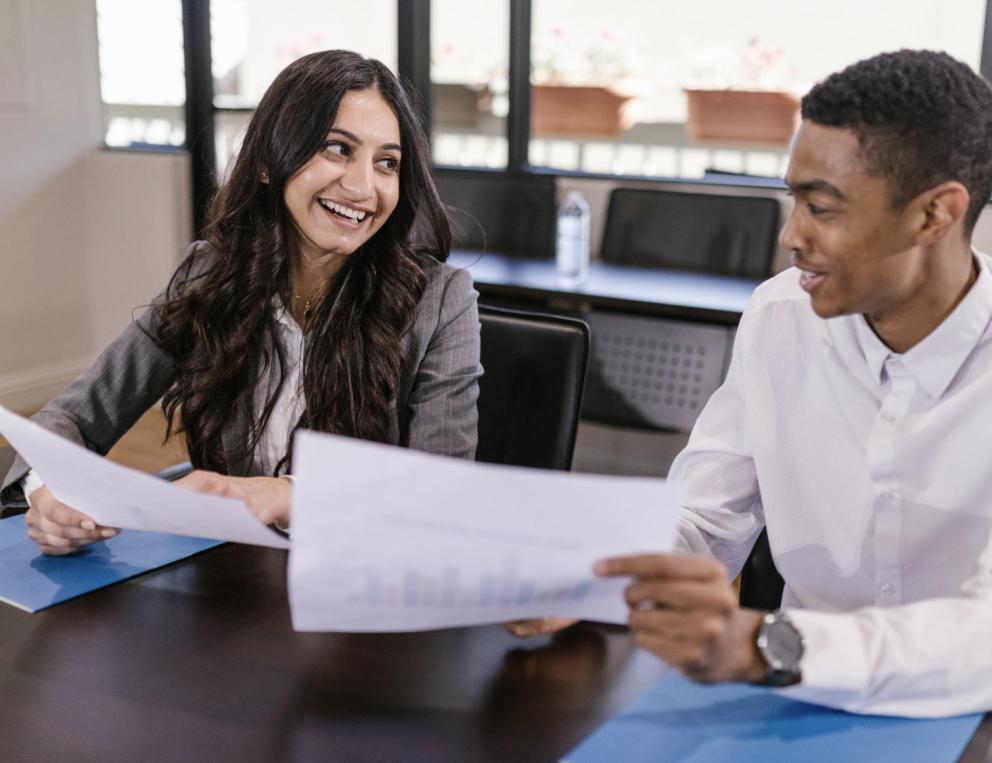 Image of two colleagues holding papers and chatting.