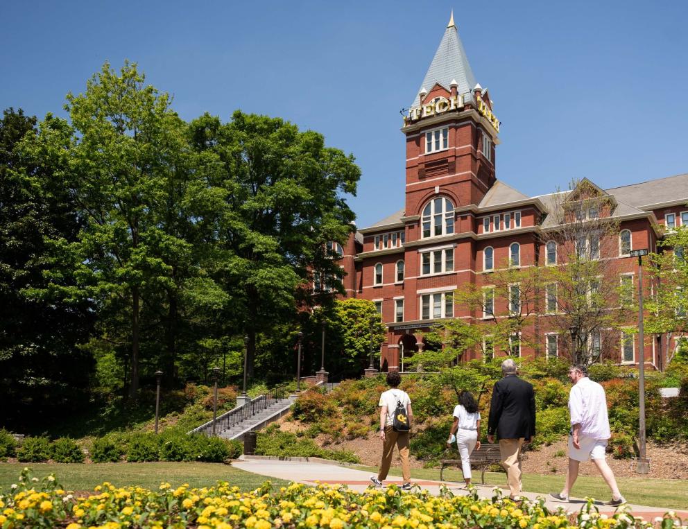 A photo of Tech Tower in spring, with faculty and a student walking in front of it.